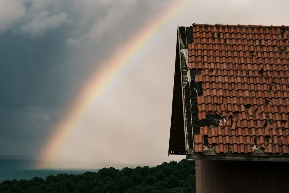A dramatic scene of a neglected rooftop with a vibrant rainbow cutting through a moody, overcast sky.